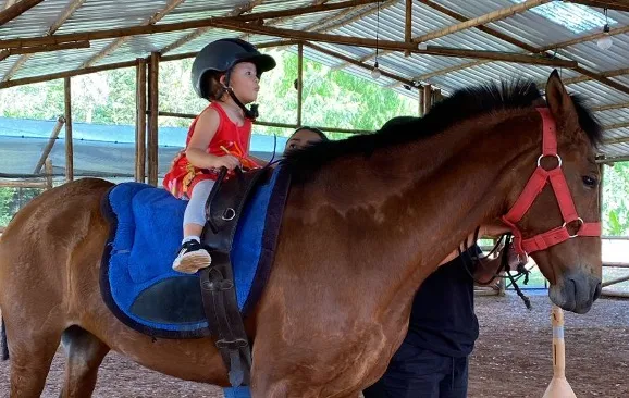 A child enjoys a horseback ride in a safe and supervised environment, an activity that can help build confidence and motor skills.