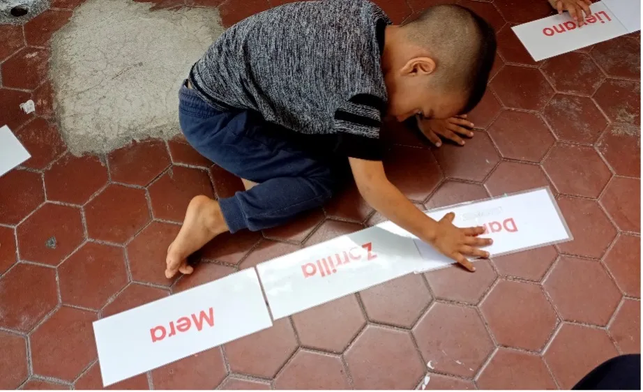 A young learner works with word cards on the floor, an activity designed to build reading fluency and vocabulary.