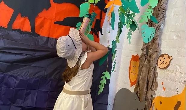 A child dressed as an explorer engages in imaginative play, looking for animals in a jungle-themed setting.